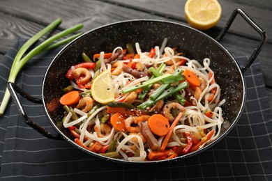 Photo of Shrimp stir fry with noodles and vegetables in wok on black wooden table, closeup