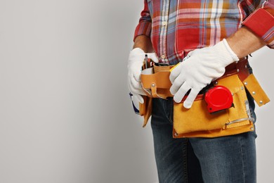 Photo of Professional builder with tool belt on light background, closeup. Space for text