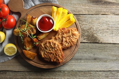 Photo of Tasty schnitzels served with potatoes, ketchup and vegetables on wooden table, flat lay. Space for text