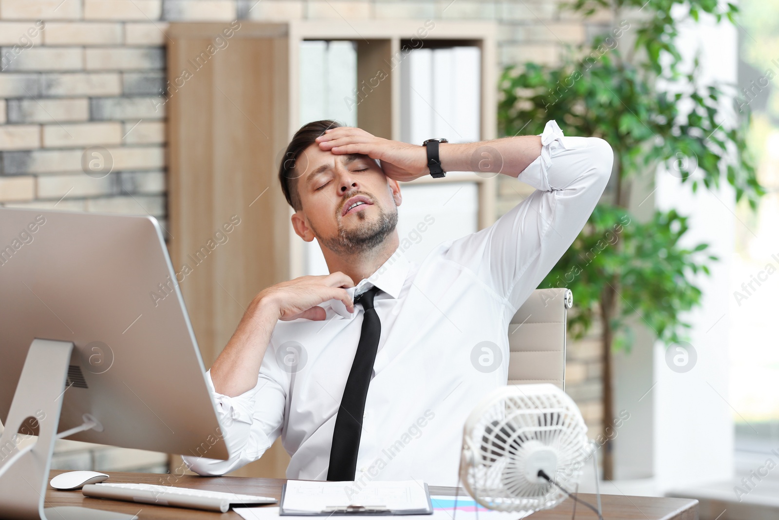 Photo of Businessman suffering from heat in front of small fan at workplace