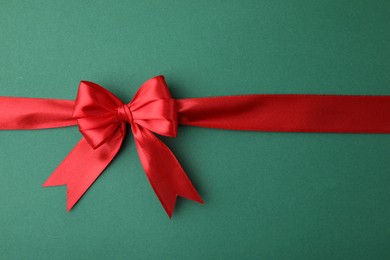 Photo of Red satin ribbon with bow on green background, top view