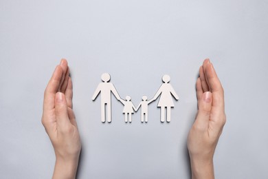 Photo of Woman protecting figures of family on light background, top view. Insurance concept