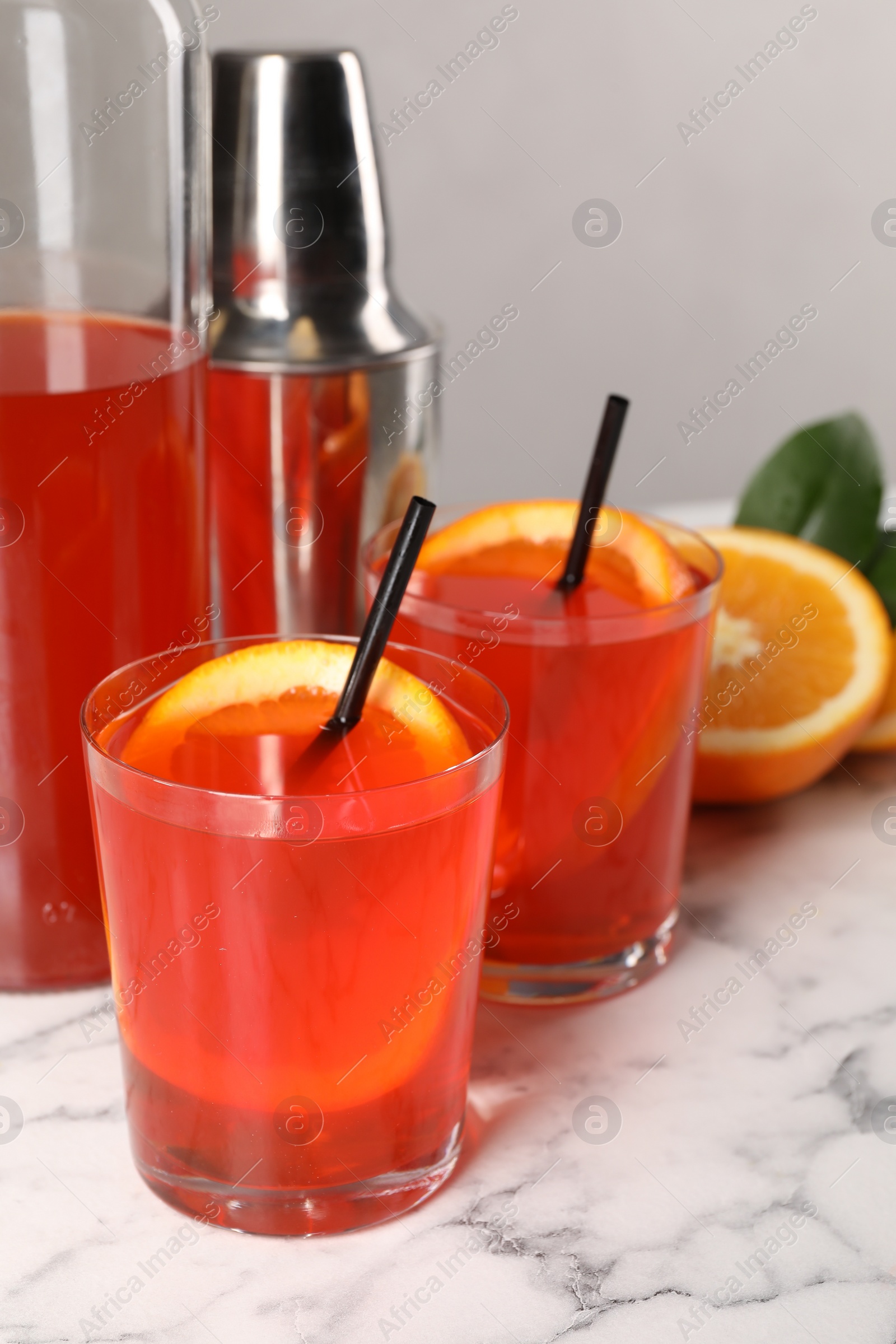 Photo of Aperol spritz cocktail, orange slices and straws in glasses on white marble table, closeup
