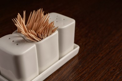 Holder with salt, pepper and toothpicks on wooden table, closeup. Space for text