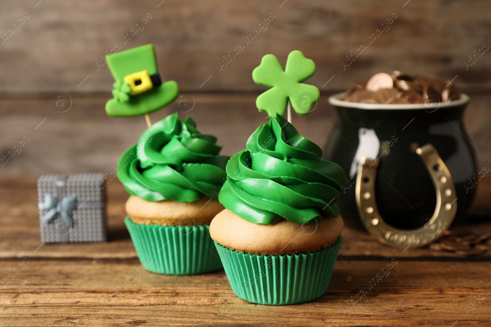 Photo of Decorated cupcakes and pot with gold coins on wooden table. St. Patrick's Day celebration