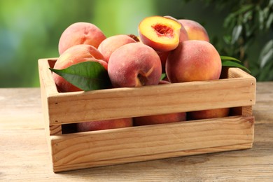 Cut and whole fresh ripe peaches in crate on wooden table against blurred background, closeup