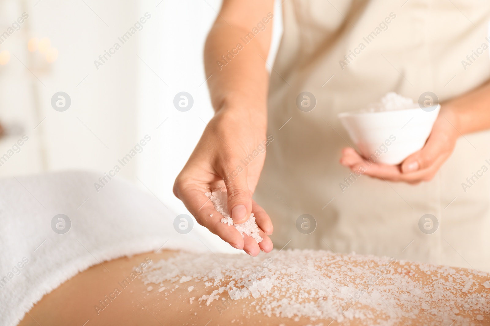 Photo of Young woman having body scrubbing procedure with sea salt in spa salon, closeup