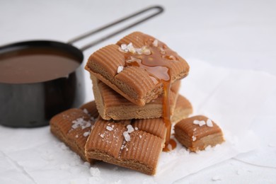 Photo of Yummy caramel candies, sauce and sea salt on white table, closeup