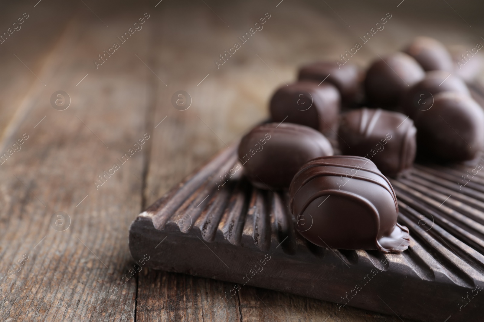 Photo of Tasty dark chocolate candies on wooden board, closeup