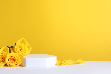 Beautiful presentation for product. Podium and roses on white table against yellow background, space for text