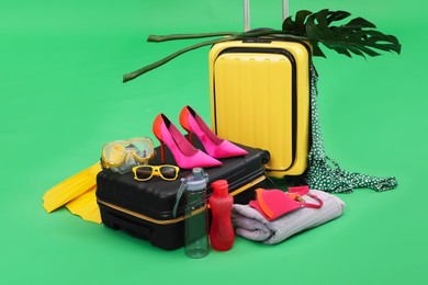 Photo of Suitcases, beach accessories and tropical leaves on green background. Summer vacation
