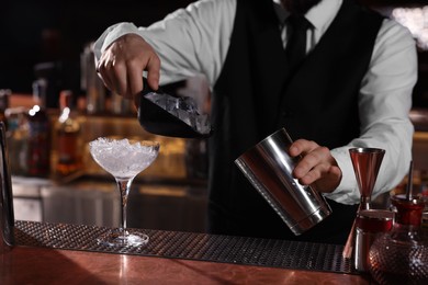 Photo of Bartender preparing fresh alcoholic cocktail in martini glass at bar counter, closeup