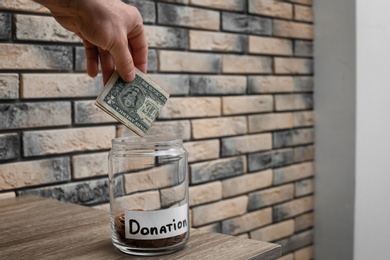 Man putting money into donation jar on table, closeup. Space for text