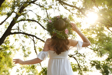 Photo of Young woman wearing wreath made of beautiful flowers outdoors on sunny day, back view