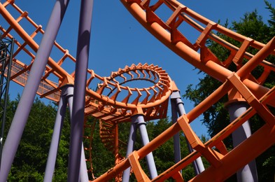 Photo of Amusement park. Beautiful colorful rollercoaster and green trees against blue sky