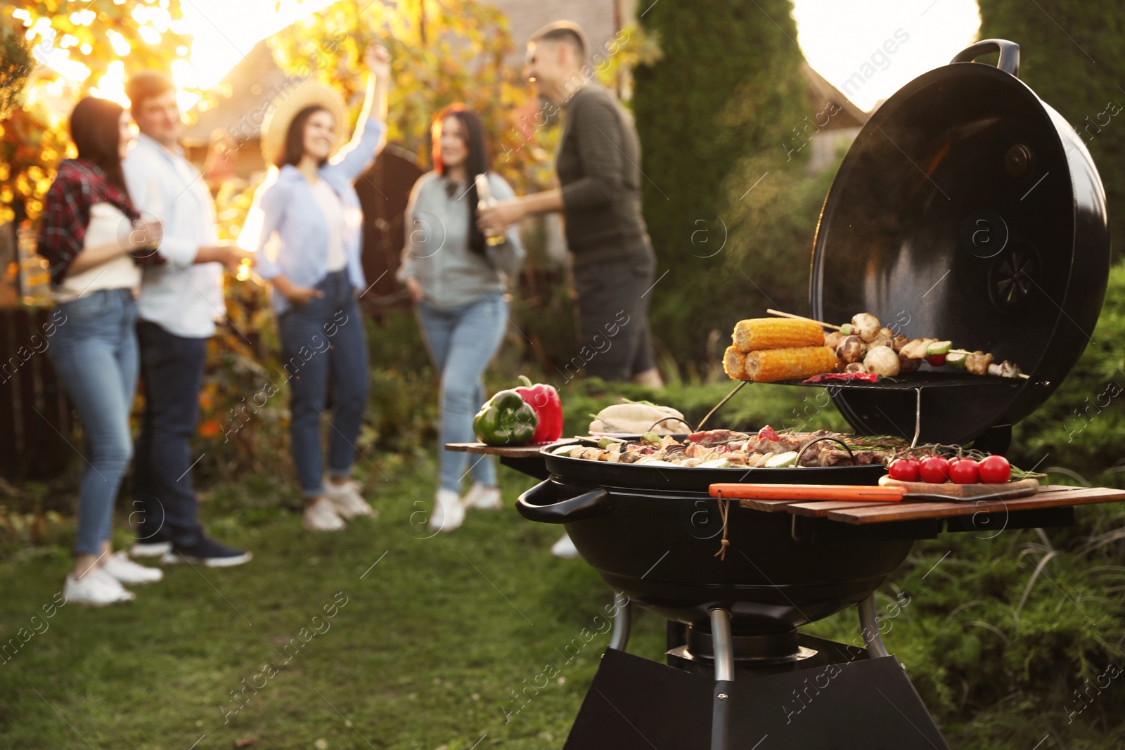 Photo of Group of friends having party outdoors. Focus on barbecue grill with food. Space for text