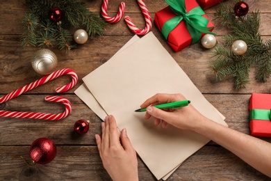 Woman writing letter to Santa Claus at wooden table, top view. Christmas celebration