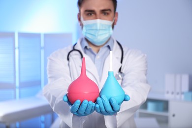 Doctor holding rubber enemas in examination room, focus on hands
