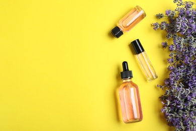 Bottles of essential oil and lavender flowers on yellow background, flat lay. Space for text