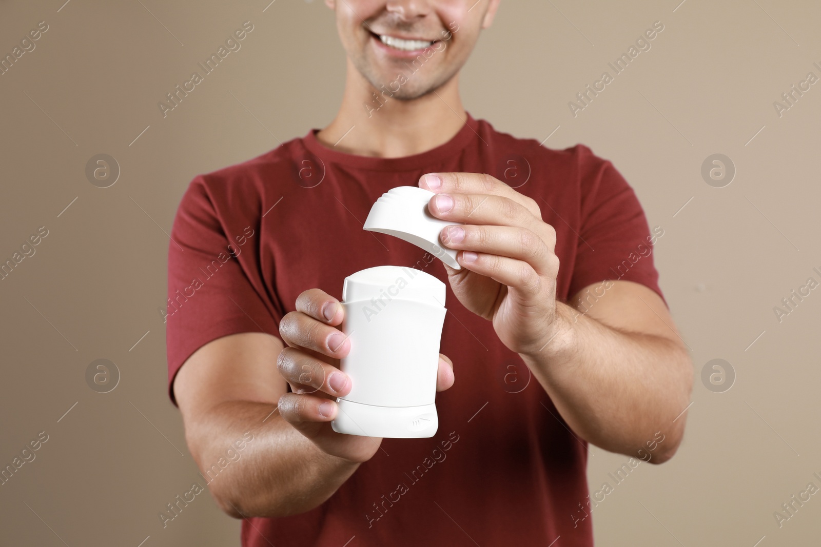 Photo of Young man holding deodorant on beige background, closeup. Mockup for design