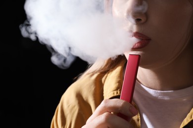 Photo of Young woman using electronic cigarette on black background, closeup