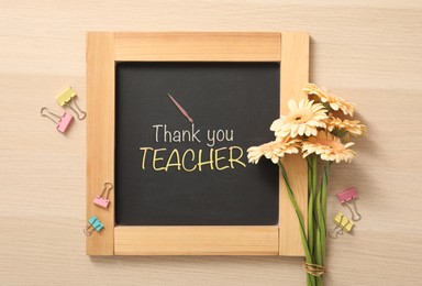 Image of Small blackboard with phrase Thank You Teacher, flowers and color paper clamps on wooden table, flat lay
