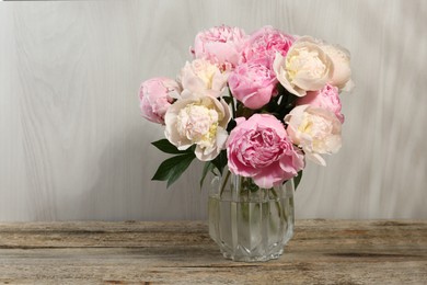Photo of Beautiful peonies in vase on wooden table, space for text