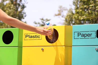 Woman throwing plastic bottle into sorting bin on city street, closeup. Recycling waste