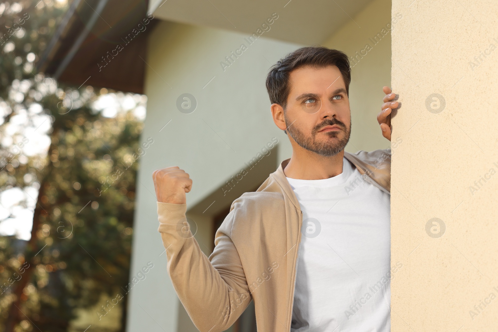 Photo of Angry man showing fist near house. Annoying neighbour