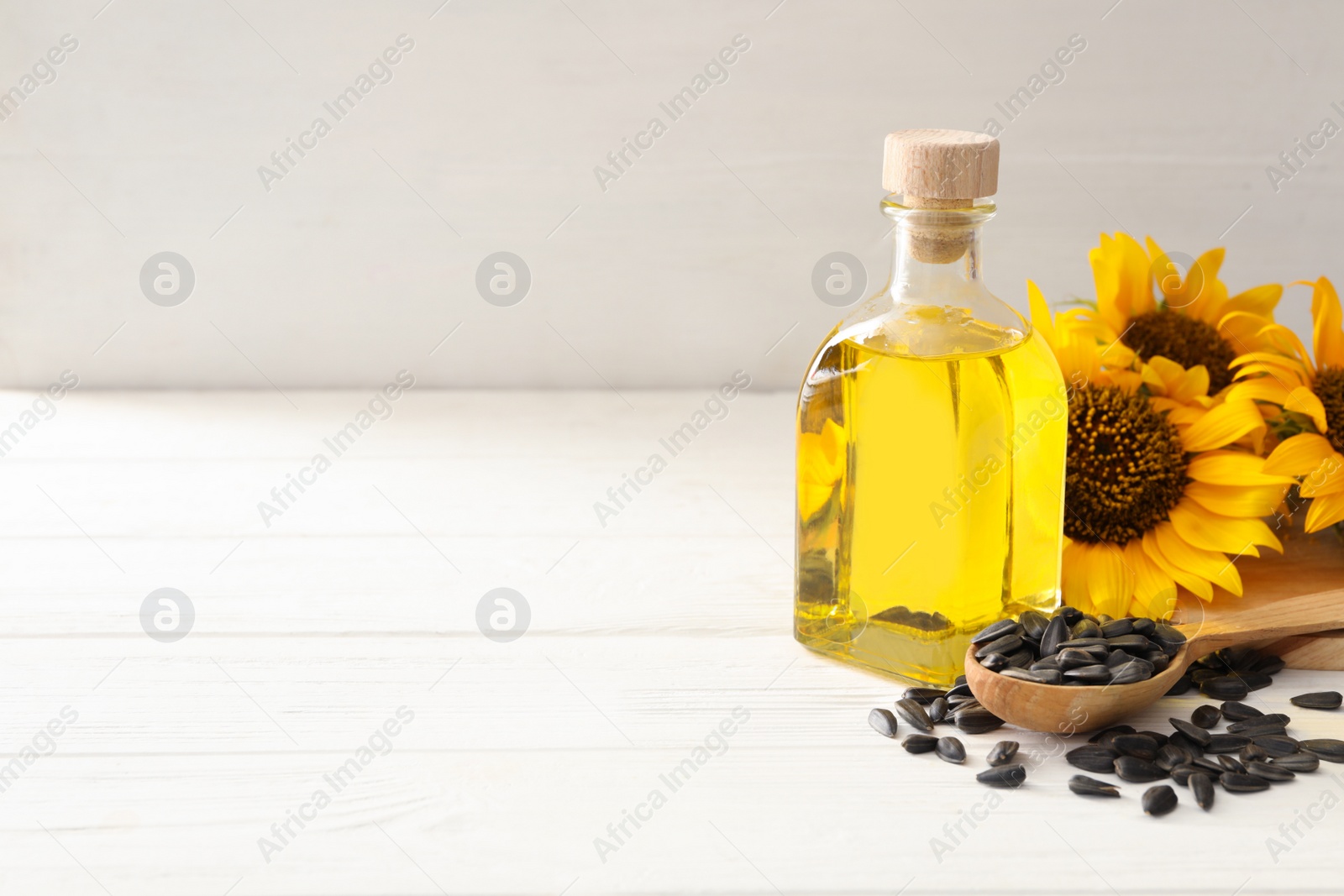 Photo of Sunflowers, bottle of oil and seeds on white wooden table, space for text