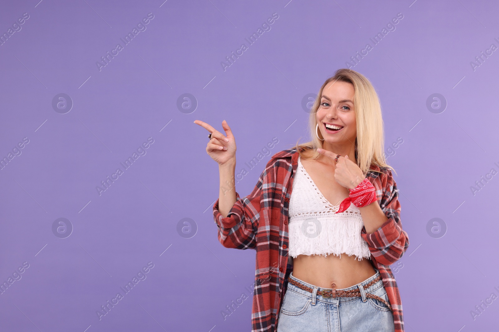 Photo of Portrait of happy hippie woman pointing at something on purple background. Space for text