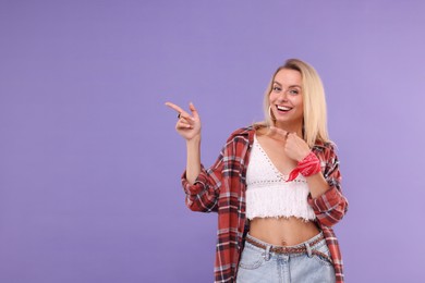 Portrait of happy hippie woman pointing at something on purple background. Space for text