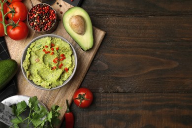 Photo of Bowl of delicious guacamole and ingredients on wooden table, flat lay. Space for text