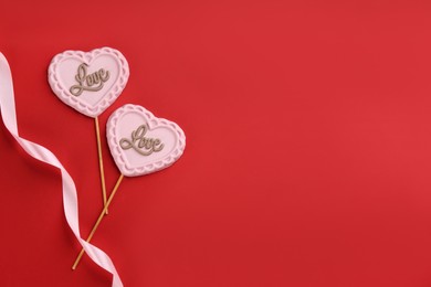 Photo of Chocolate heart shaped lollipops and ribbon on red background, flat lay. Space for text