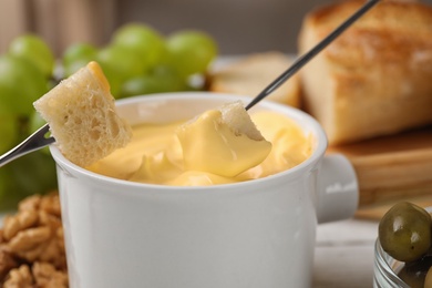 Dipping pieces of bread into tasty cheese fondue on table, closeup view