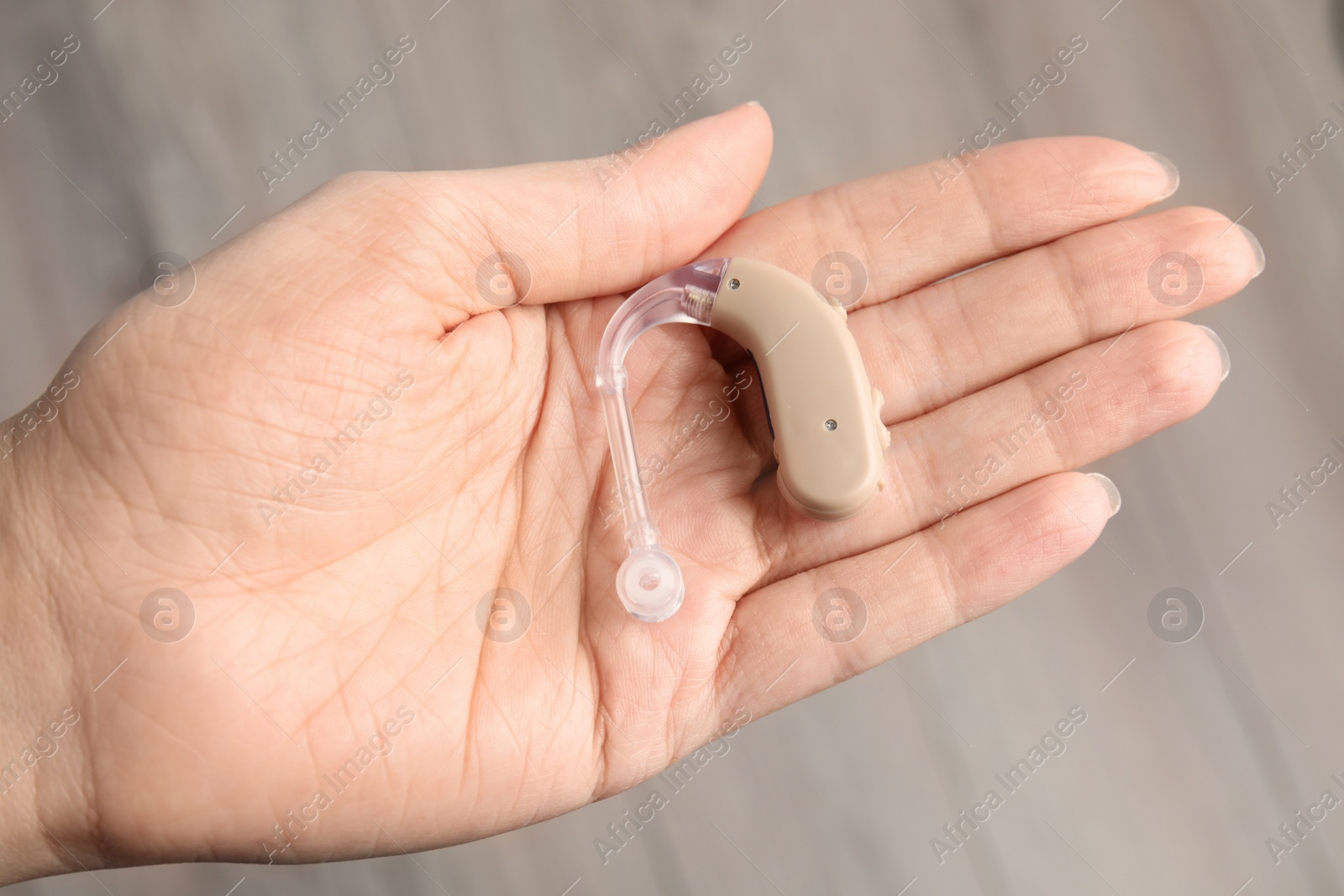 Photo of Woman holding hearing aid on blurred background, closeup