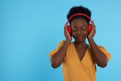 Photo of Beautiful young woman in headphones enjoying music on light blue background. Space for text