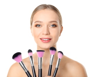 Portrait of beautiful young woman with makeup brushes on white background