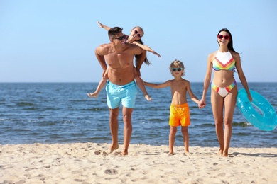 Happy family with inflatable ring on sandy beach near sea. Summer holidays