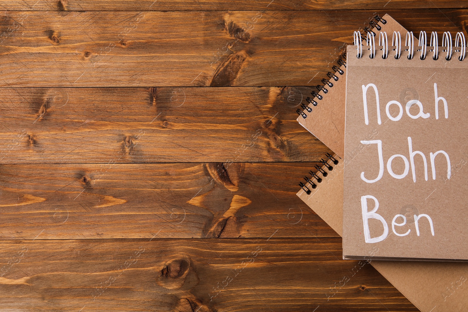 Photo of Notebook with different baby names on wooden table, flat lay. Space for text