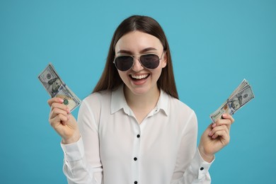 Happy woman with dollar banknotes on light blue background