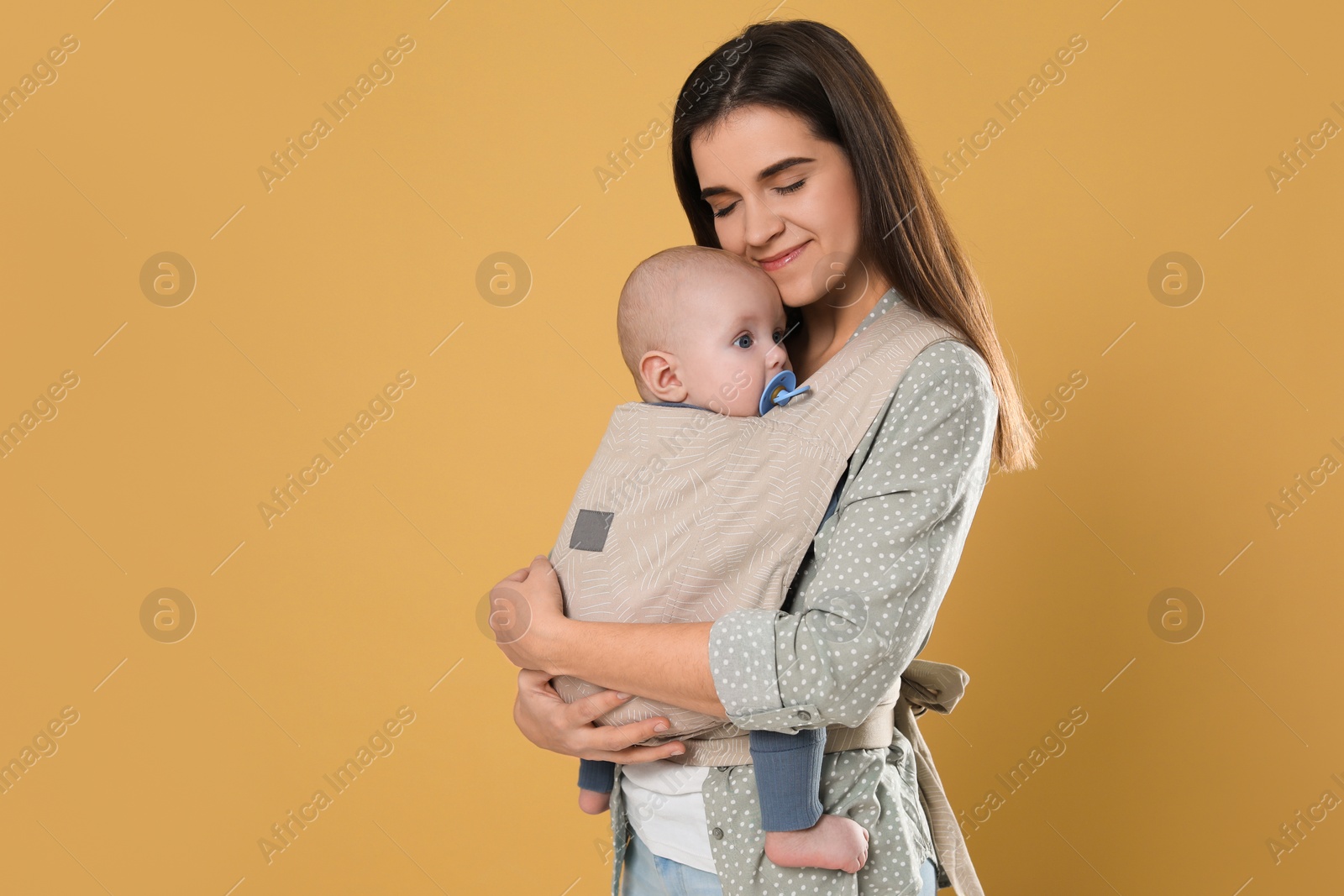 Photo of Mother holding her child in sling (baby carrier) on beige background. Space for text