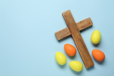 Wooden cross and painted Easter eggs on light blue background, flat lay. Space for text