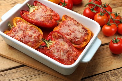 Photo of Tasty stuffed peppers in dish and ingredients on wooden table