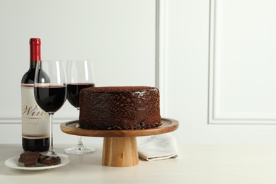 Photo of Delicious truffle cake, chocolate pieces and red wine on light wooden table, space for text