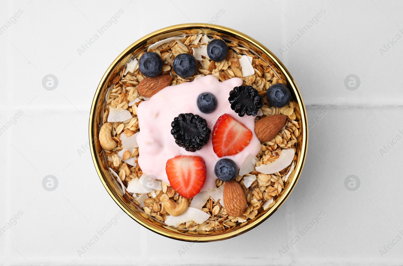 Photo of Tasty granola, yogurt and fresh berries in bowl on white tiled table, top view. Healthy breakfast