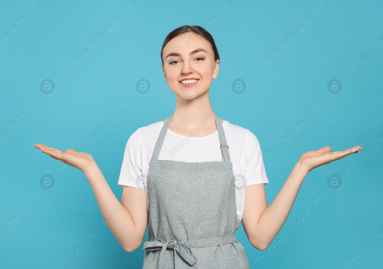 Photo of Beautiful young woman in clean apron with pattern on light blue background