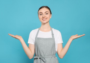 Beautiful young woman in clean apron with pattern on light blue background