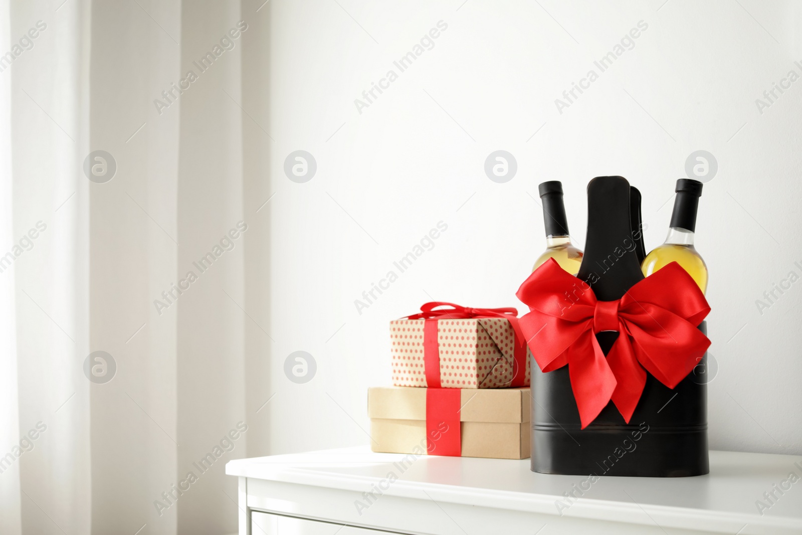 Photo of Bottles of wine in holder with bow and gift boxes on table in light room. Space for text