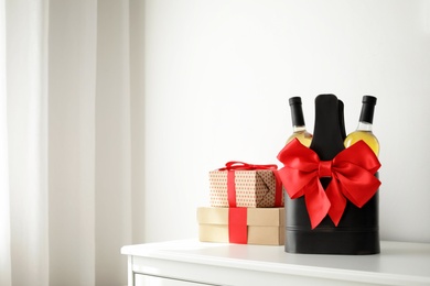 Bottles of wine in holder with bow and gift boxes on table in light room. Space for text